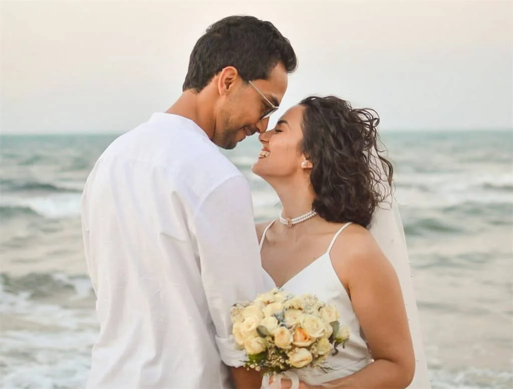 海辺で結婚式の衣装を着たカップルが甘い視線を交わし、花嫁が花束を手にした